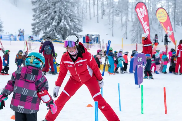 Skilehrerin übt mit einem Kind im Skikindergarten zwischen bunten Stangen